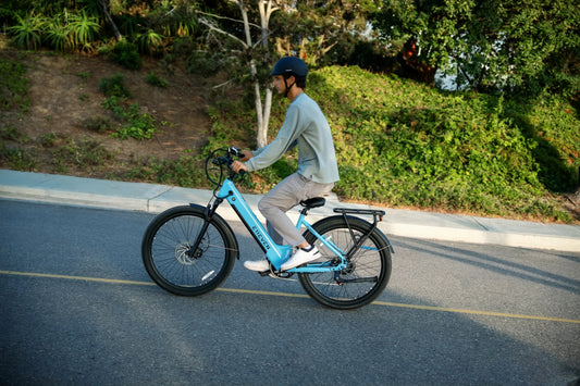 Rider on an E11EVEN DRAGONFLY Lightweight e-Bike cruising along a paved road surrounded by greenery.