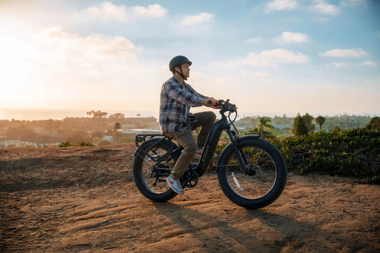 Rider on an E11EVEN DEFIANT fat tire electric bike riding along a dirt trail at sunset.