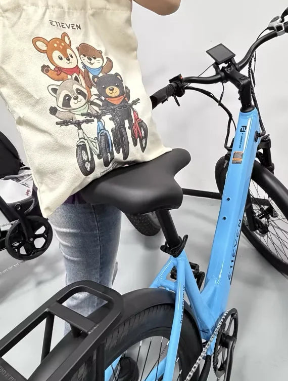 E11EVEN mascot tote bag beside a blue step-through electric bike and rear rack.