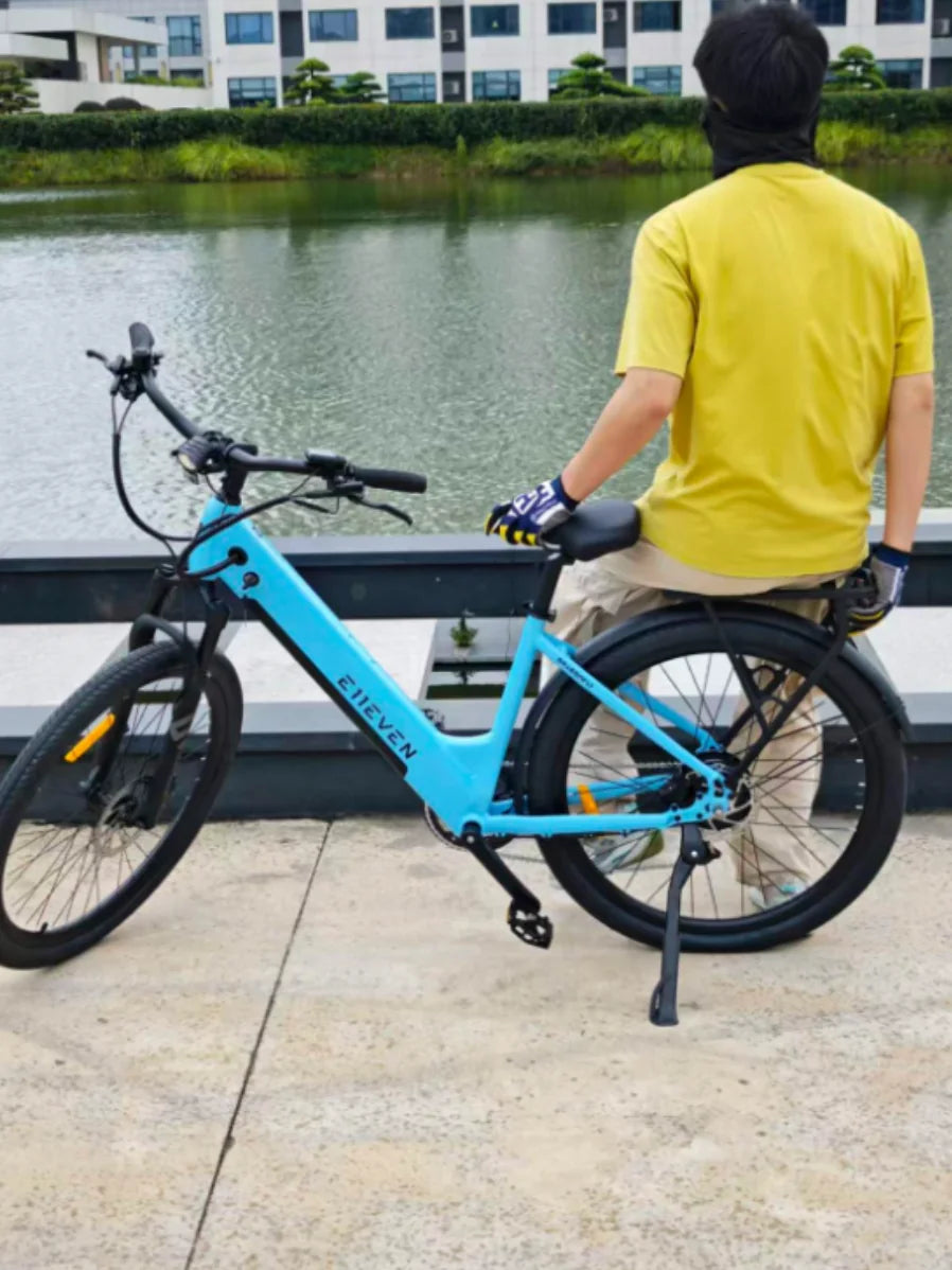 Rider in a yellow shirt on a blue E11EVEN step-through electric bike beside a lake.
