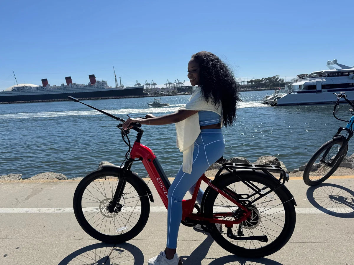 Rider with a red E11EVEN step-through electric bike on a waterfront path.
