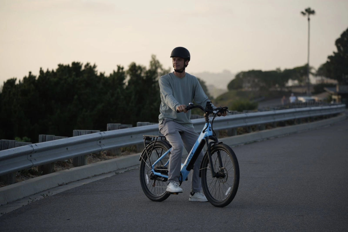 Man riding a white commuter ebike on a paved road beside a guardrail