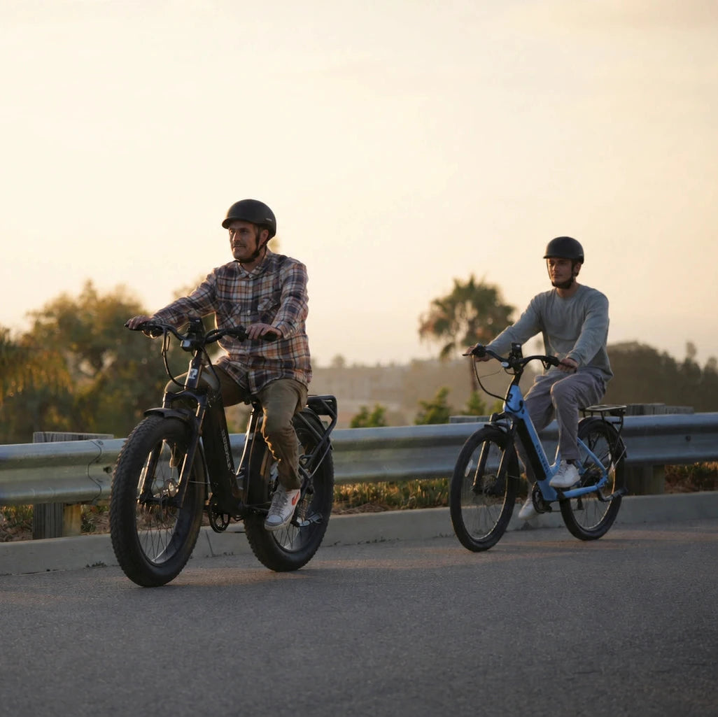 Two riders on black and white ebikes traveling along a road at sunset