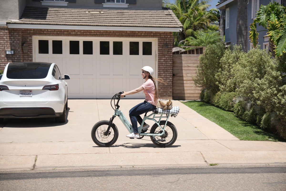 Woman riding a white compact ebike on a suburban driveway with a garage in the background