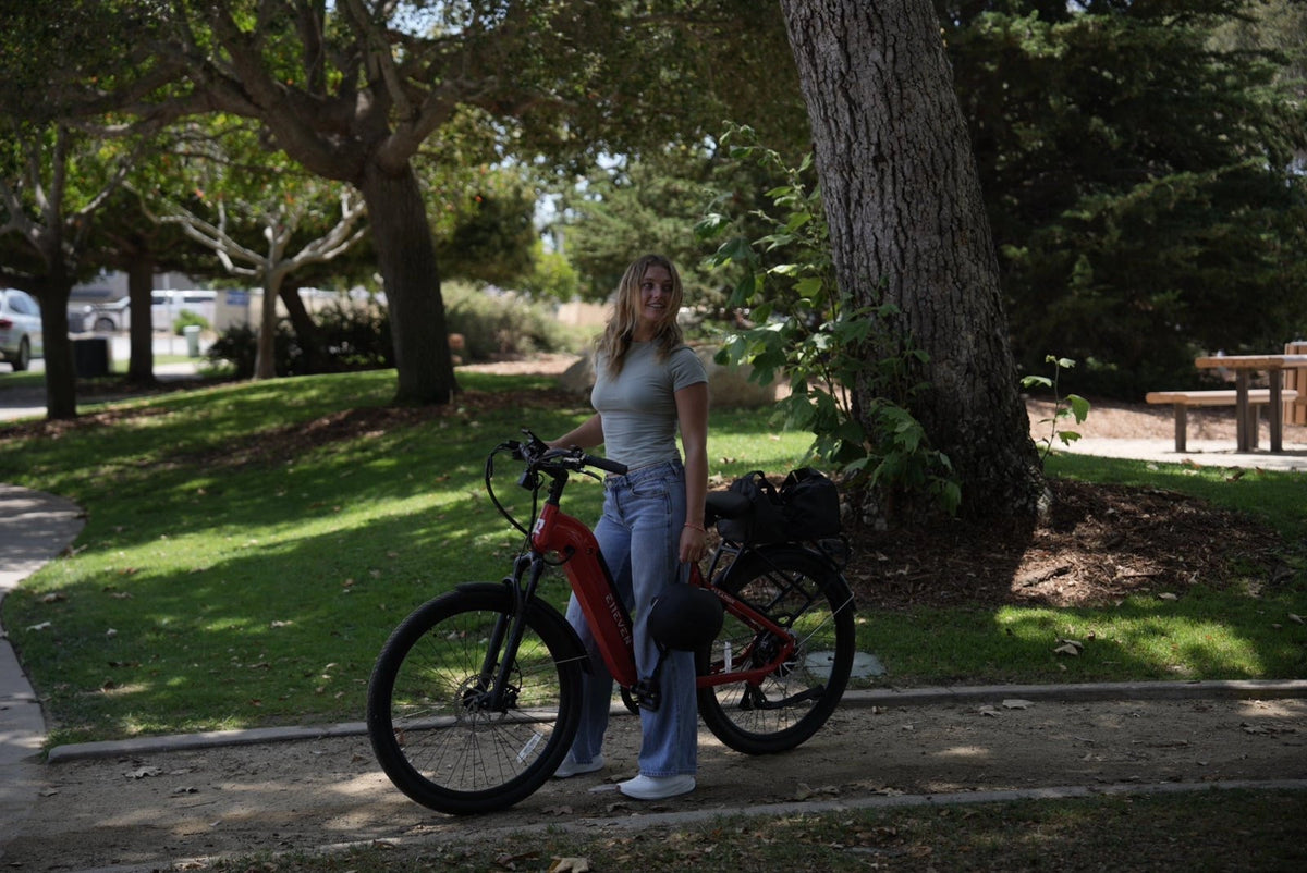 Woman standing beside a red step-through ebike on a shaded park path near trees